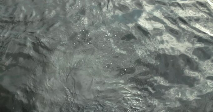 Top down view of rippling sea water with reflections and small white bubbles.