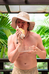 Scandinavian Tourist Man Eating Durian Outdoors with Tropical Leaves Background