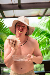 Scandinavian Tourist Man Eating Durian Outdoors with Tropical Leaves Background