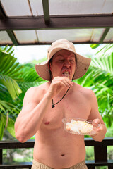 Scandinavian Tourist Man Eating Durian Outdoors with Tropical Leaves Background