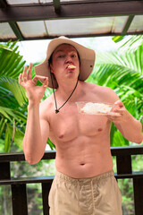 Scandinavian Tourist Man Eating Durian Outdoors with Tropical Leaves Background
