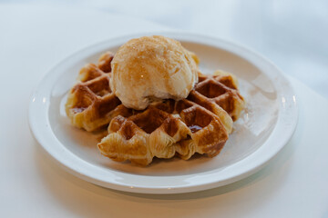 Waffles topped with a scoop of smooth ice cream, drizzled with sweet syrup on a white ceramic plate.