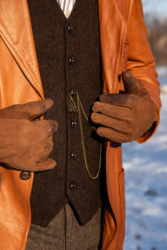 Retro aesthetics, male fashion details. Leather trench coat and gloves, vintage wool waistcoat and pocket watch chain with the train-shape pendant. Abstract.