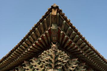 Ornate roof of a traditional building with intricate details, featuring a carved dragon motif against the sky. © heerim studio