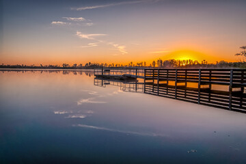 Fototapeta premium A dock is on the water with a sunset in the background. The water is calm and the sky is orange