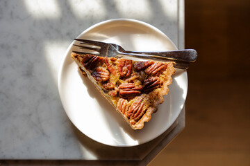 Delicious pecan pie slice on a white plate with fork, bathed in warm sunlight, a tempting dessert...