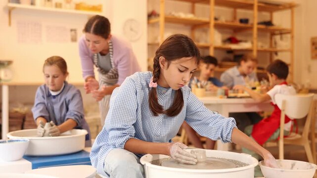 Pleased underage attendees of pottery circle working at throwing-wheel with female instructor