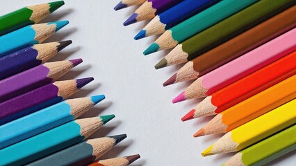 Fototapeta premium Bright colored pencils are arranged in two groups diagonally on a white background, creating a beautiful contrast and inspiring creativity and drawing.