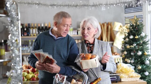 Elderly married couple is looking at sweets in store. Market visitors choose from several deserts, consider nougat, panellets, marzipan. Customers choose national European sweet desserts in sales area