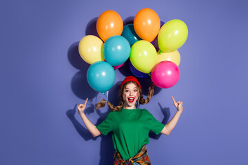 Happy young girl with colorful balloons smiling against purple background