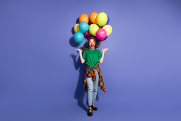 Young girl joyfully holds colorful balloons against a purple studio backdrop creating a playful...