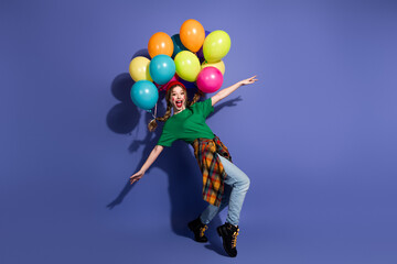 Joyful young girl with colorful balloons on bright purple backdrop wearing green shirt jeans and...