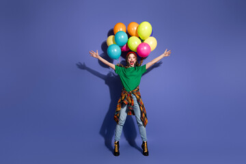 Young woman jumps with colorful balloons against purple background creating a fun joyful...