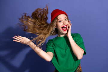 Young girl beanie shirt flowing hair shoots lively purple background smiling broadly showing energy...