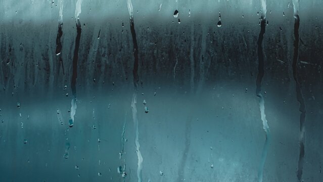 Window pane covered in condensation and raindrops, creating a blurred, abstract surface