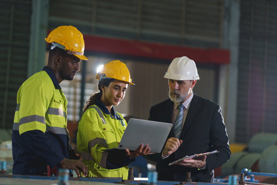 Multicultural industrial engineers reviewing project on laptop in factory control room
