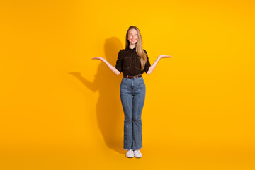 Young female model stands against a bright yellow background with a friendly smile and open arms...