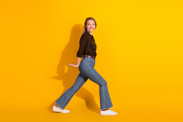 Young woman in casual jeans black shirt walking on yellow background smiling
