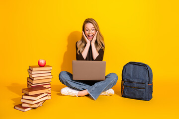 Young student girl surprised by her laptop moment with book and backpack on a bright yellow...