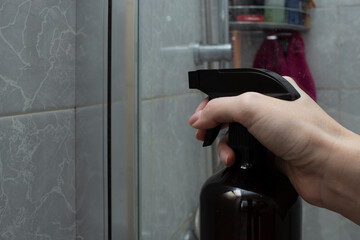Woman spraying cleaner on shower glass