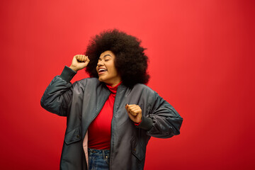 Joyful stylish woman dancing against a vibrant red backdrop with confidence and flair