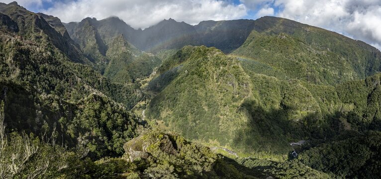 Densely overgrown steep mountains with rainbow, green mountain landscape, view from Miradouro dos Balc&otilde;es, mountain valley Ribeira da Metade and the central mountains, Madeira, Portugal