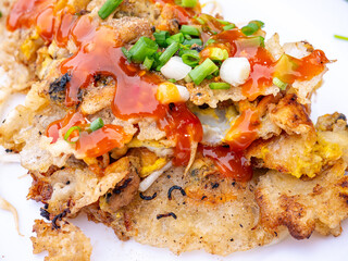 Crispy Thai Oyster Omelette (Hoi Tod) topped with sweet chili sauce and fresh spring onions on a white plate