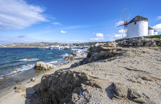 Windmills on the coast, Kato Milli, beach with sand and rocks, white Cycladic houses in the back, houses of Little Venice, Mykonos, Greece
