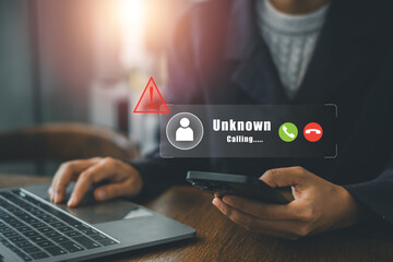 Businessperson at desk receiving unknown call alert on smartphone while using laptop, highlighting communication and technology.