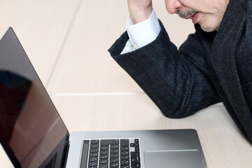 ノートPCの前で悩むスーツ姿のシニア男性