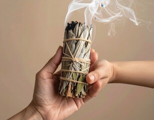 Close Up Of Hands Holding Smudging Stick With Smoke Rising Against Beige Background