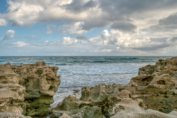The ocean is calm and the sky is cloudy. The rocks on the shore are large and jagged