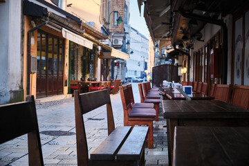 Perspective view of outdoor cafe with wooden tables and chairs arranged along narrow stone-paved street in Bascarsija historic district in Sarajevo, Bosnia and Herzegovina