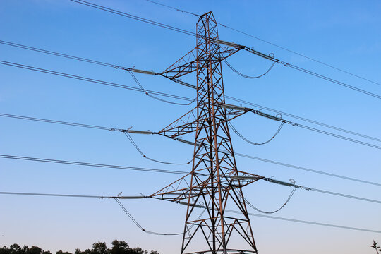 Large steel lattice transmission tower set against a clear blue sky, supporting multiple high-voltage power lines via long glass insulators.