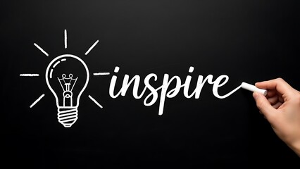 Hand drawing the word inspire next to a bright idea lightbulb sketch using white chalk on a dark textured blackboard surface for creative concept