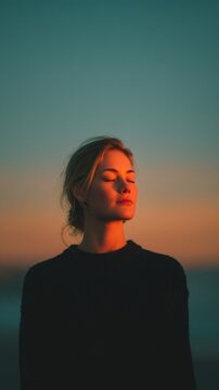 One young European woman with closed eyes calmly facing sunset light in peaceful outdoor scene, vertical photo
meditation, mindfulness, self care, relaxation, mental health, nature, peace, emotional 