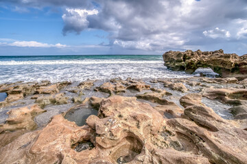A rocky beach with a cloudy sky in the background. The beach is calm and peaceful, with the waves gently lapping at the shore. The rocks on the beach are scattered throughout, creating a rugged