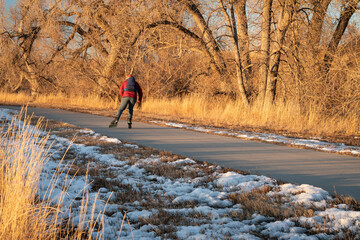 senior male with backpack is inline skating on a paved bike trail along Poudre River in Colorado, fall or winter scenery at sunset © MarekPhotoDesign.com
