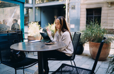 Asian freelancer sits outdoors with tablet and stylus, calmly navigating screen. Portrays remote work culture, tech fluency, and mobile autonomy in digital age.