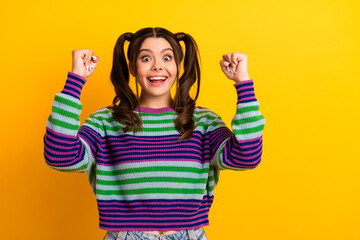 Young woman with colorful striped sweater celebrates with a joyful smile against a bright yellow...