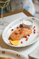 Grilled salmon steak served with creamy sauce citrus slice and herbs on elegant plate at restaurant table