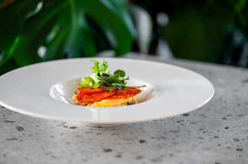 A gourmet appetizer of layered tomato and possibly cured meat or cheese tartare with fresh green garnish, served on a modern white plate in a restaurant setting