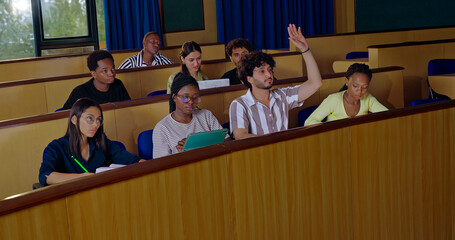 Indian young adult gen z pupil smart girl boy guys sitting desk table hold pencil exam notes book work class room. Teen female learn new study male man talk raise hand share plan ideas day hall place