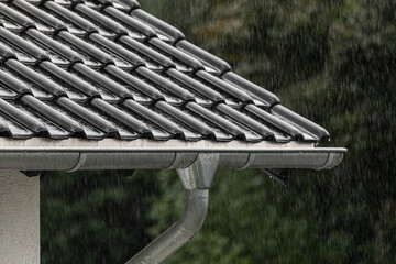 Corner of roof with black tiles and rain gutter in heavy rainfall
