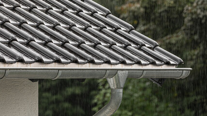 Rainy roof corner with black tiles, gutter and downspout, 16:9

