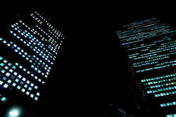 夜景を捉えた都会の高層ビル群。無数の窓明かりが点滅し、暗闇に浮かび上がる近未来的な都市景観。