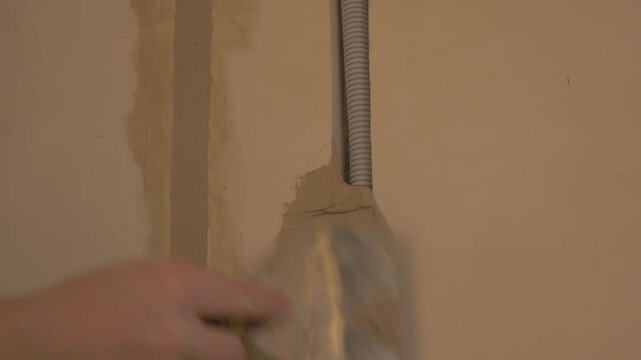 Electrician applying plaster to wall surface with putty knife, smoothing out imperfections in preparation for finishing touches. Electrician concept