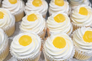 Delicious cupcakes with white cream and yellow fruit on top, closeup