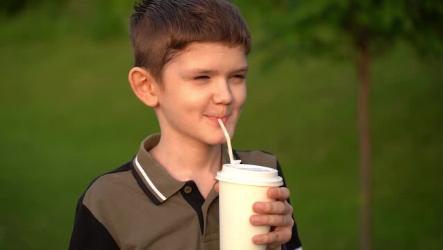 Boy drinks coffee through a straw from a disposable paper cup on outdoors.