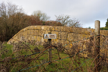 Danger Keep Out sign on disused stone canal bridge crossing Somerset Coal Canal